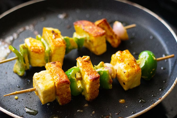 Las brochetas de paneer tikka se fríen en la sartén hasta que estén doradas