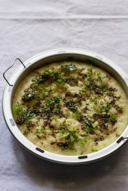 rava dhokla in steamer pan topped with the fried herbs and spices tempering mixture.