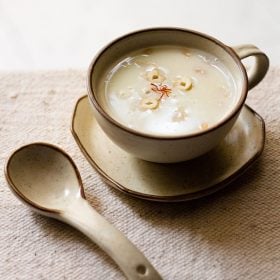 sabudana kheer served in a cream colored ceramic cup on a ceramic plate with a spoon kept on the left side.