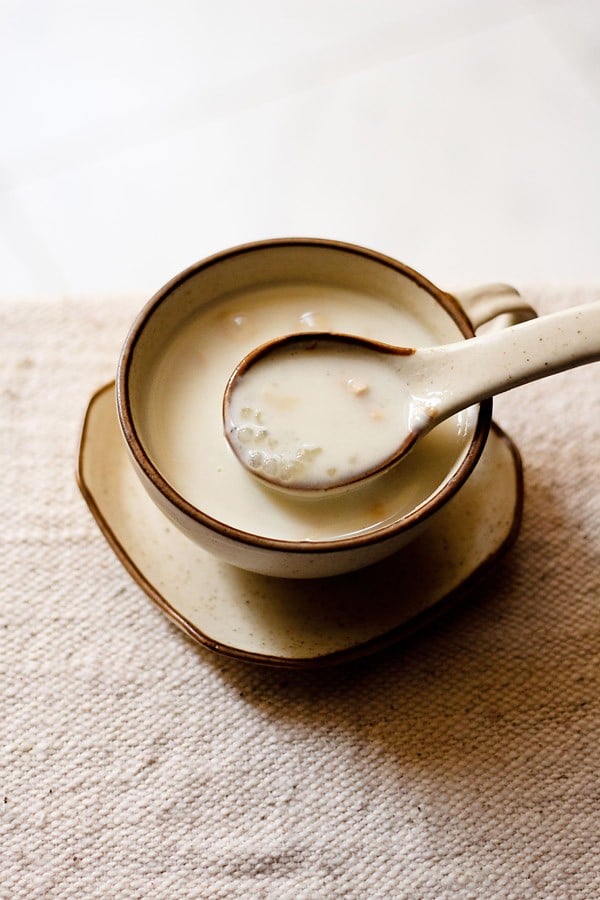 sabudana kheer in a cream colored ceramic spoon on top of ceramic cup with the sago kheer in it. 