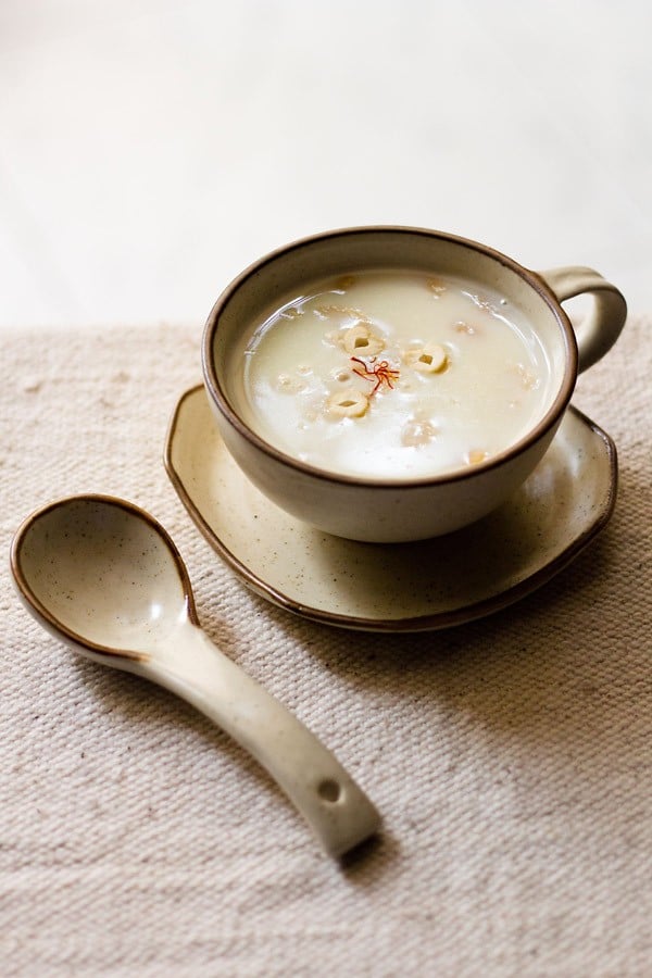 sabudana kheer served in a cream colored ceramic cup on a ceramic plate with a spoon kept on the left side.