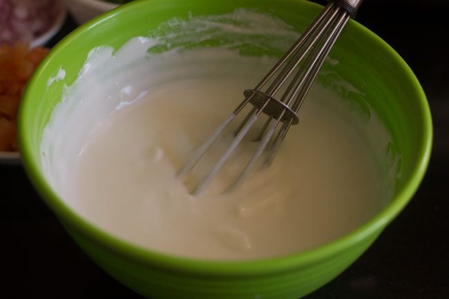 whisking curd in a bowl for making mix veg raita. 