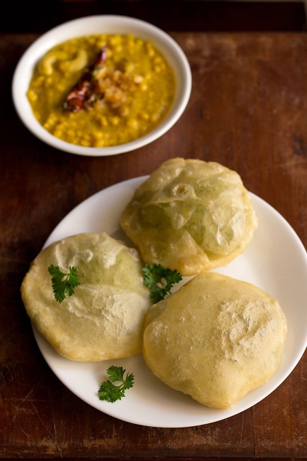 koraishutir kochuri served on a white plate with a bowl of cholar dal kept on the top left side.