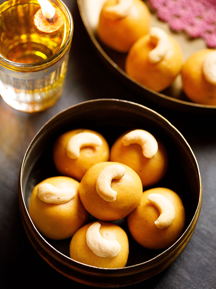 besan ke laddu placed in a brass container and a glass diya (glass lamp) on the top left side