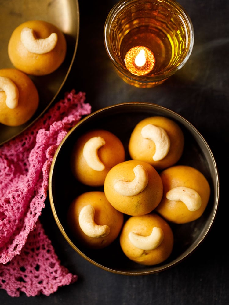 besan ke laddu placed in a brass container with a dark pink doily at the side and a glass diya on the top