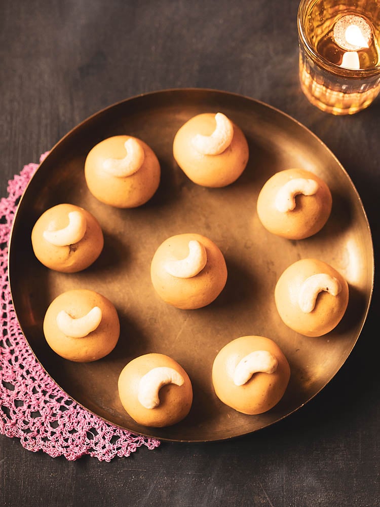 besan laddu kept in a round circle on a round brass plate on a dark pink doily