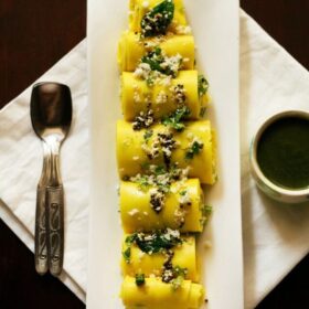 top shot of khandvi rolls garnished with fresh grated coconut and coriander leaves and served on a white platter.