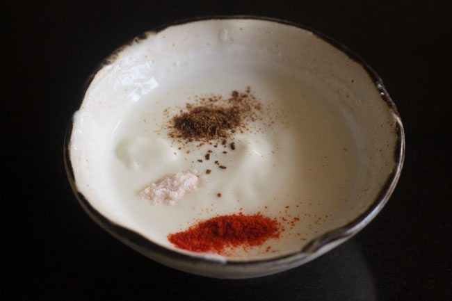 roasted cumin powder, red chili powder and rock salt added to whisked curd for making fruit raita. 