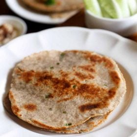 kuttu ka paratha served on a white plate with a side of peanuts cucumber and raita.