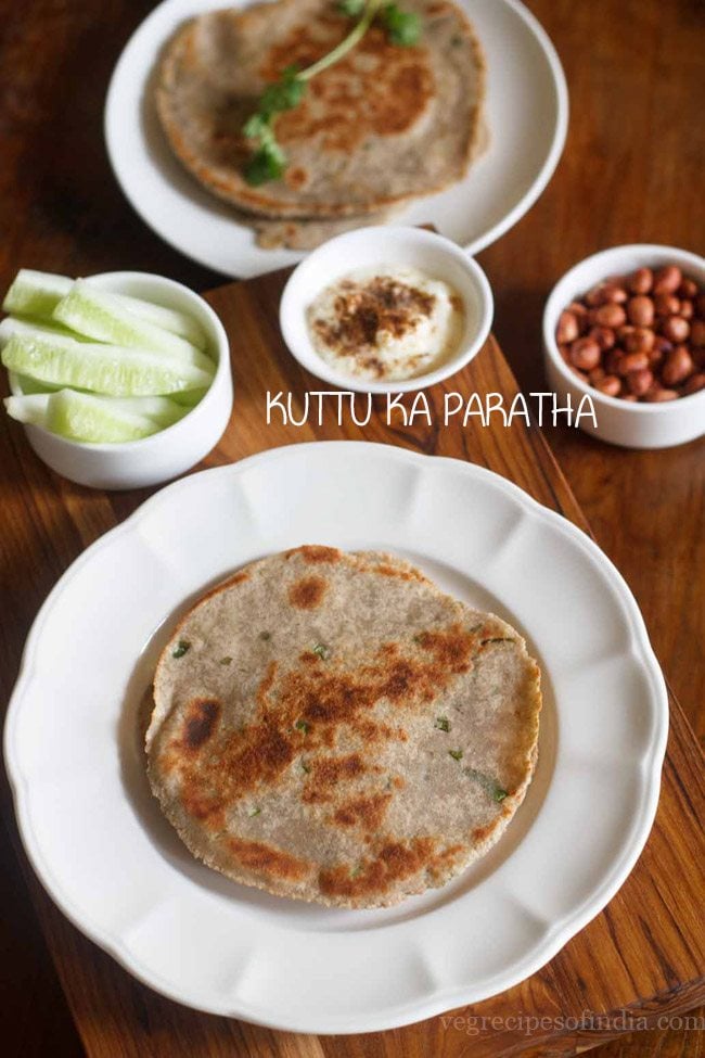 kuttu ka paratha served on a white plate with a side of peanuts cucumber and raita