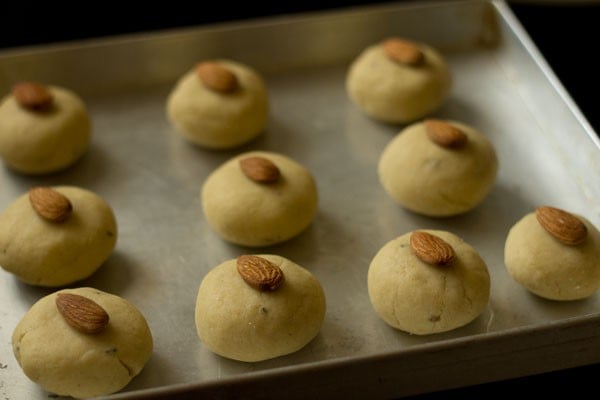 raw nankhatai dough balls with single almond placed on top lined on baking sheet.
