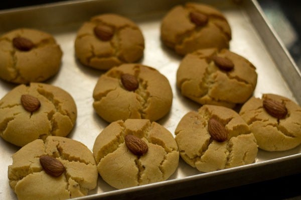 top shot of baked nankhatai biscuits with a single almond garnish on baking sheet.