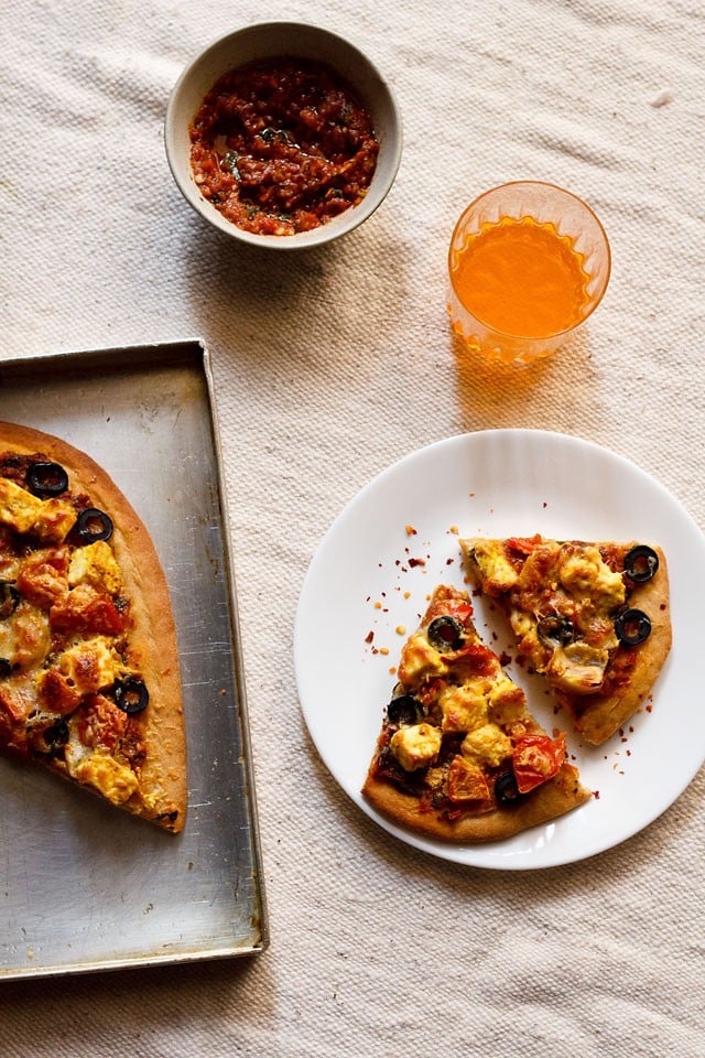 paneer tikka pizza wedges served on a plate with a glass of orange juice and dip in a bowl kept on the side.  