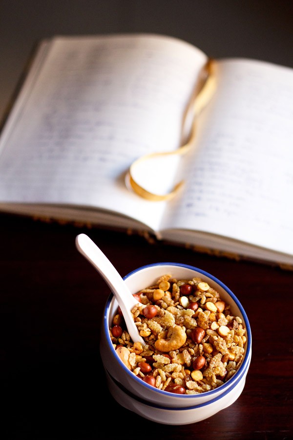 poha chiwda in a blue rimmed white bowl with a white spoon inside and an open diary behind