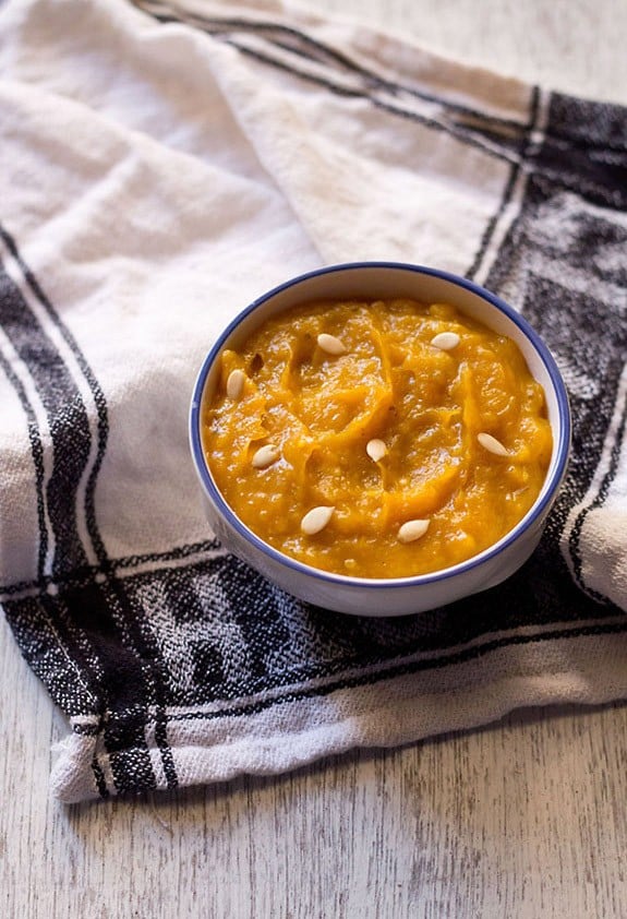 kaddu ka halwa garnished with melon seeds and served in a blue rimmed white bowl. 