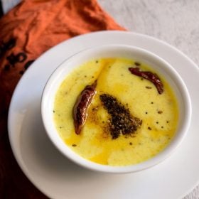 rajasthani kadhi served in a white bowl placed on top of a white plate.