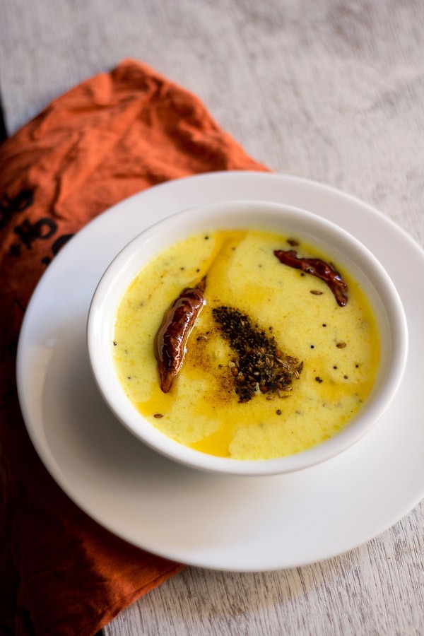 rajasthani kadhi served in a white bowl placed on top of a white plate.