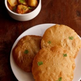 rajgira puri garnished with coriander leaves and served on a white plate with a bowl of all ki sabji in the background.