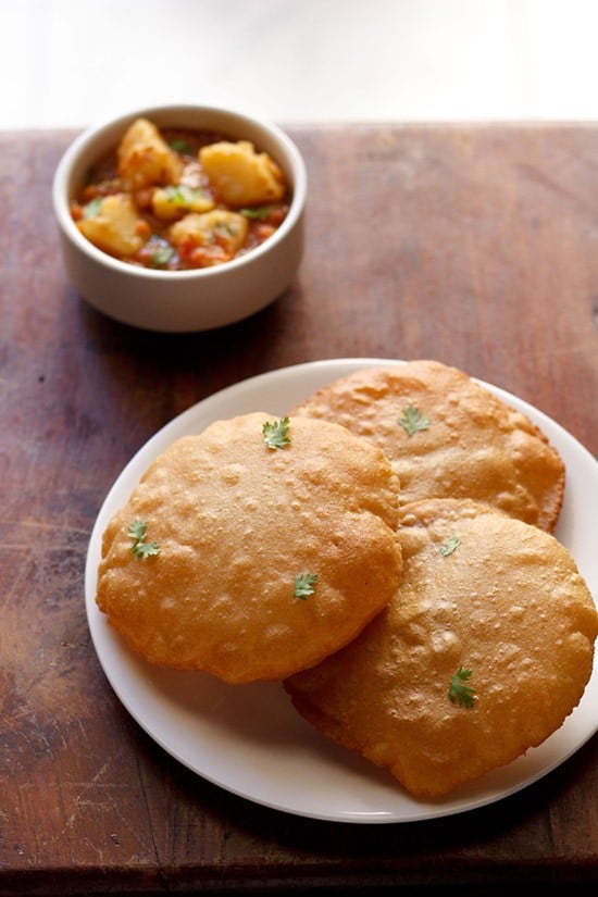 rajgira puri garnished with coriander leaves and served on a white plate with a bowl of all ki sabji in the background. 