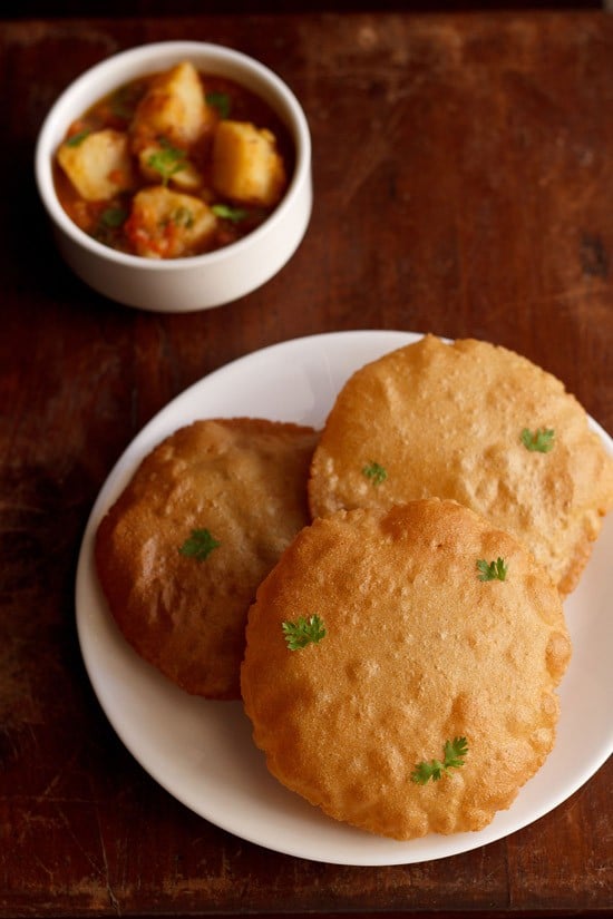 rajgira puri garnished with coriander leaves and served on a white plate with a bowl of all ki sabji in the background.