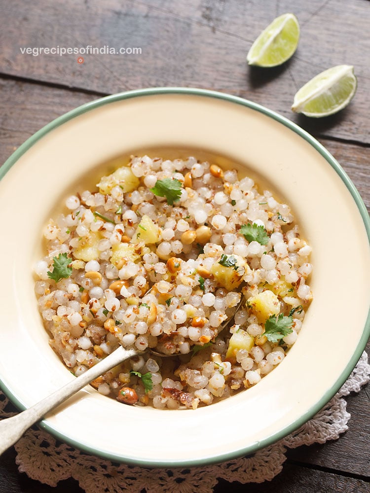 sabudana khichdi served in a green rimmed cream colored plate with a brass spoon. 