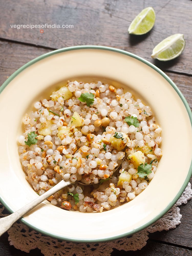 sabudana khichdi served in a green rimmed cream colored plate with a brass spoon.