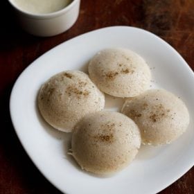 sama chawal idli served on a square white plate with a small bowl of coconut chutney kept on the top left side.