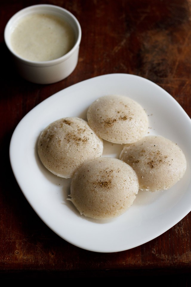 sama chawal idli served on a square white plate with a small bowl of coconut chutney kept on the top left side.