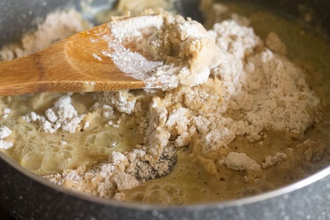 mixing wheat flour well with a wooden spatula for wheat halwa. 