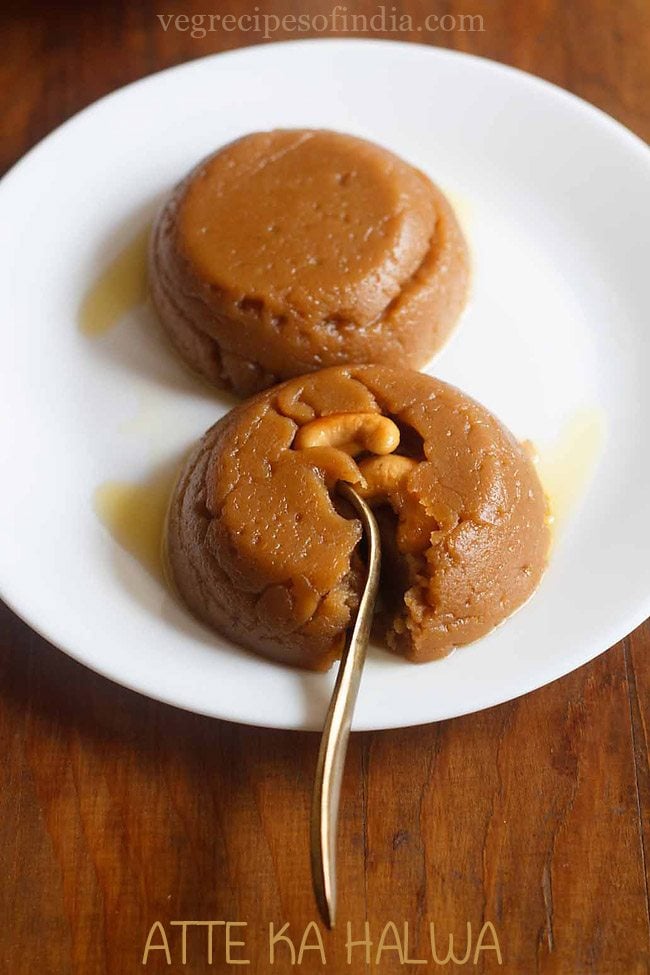 wheat halwa garnished with cashews and served on a white plate with a spoon in it and text layovers. 