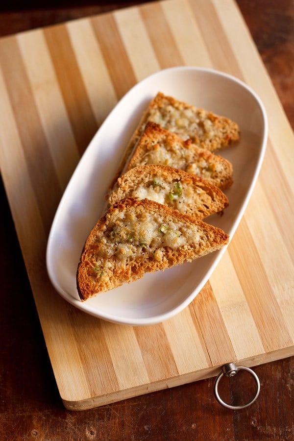 4 triangles of cheese chilli toast on an oblong white serving platter.