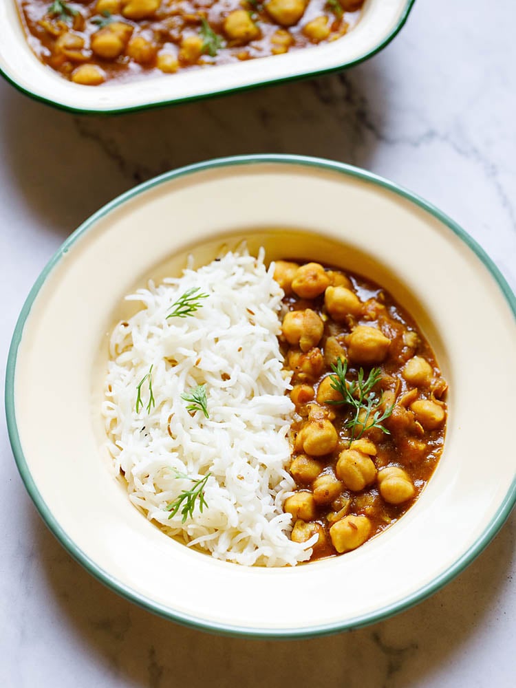 Instant Pot Chana Masala in a shallow plate with cumin rice by the side garnished with coriander sprigs