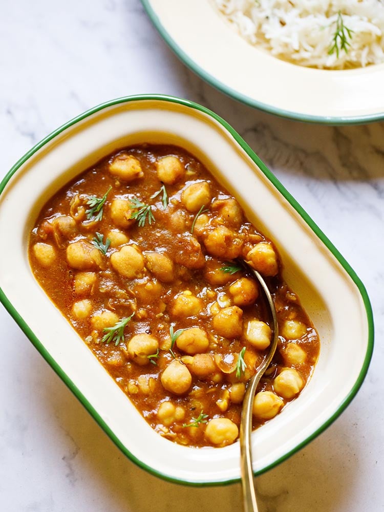 Instant Pot Chana Masala served in a rectangular enamel cream bowl with a green border with a brass spoon inside the bowl