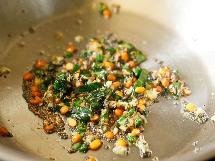 frying the spices and lentils in pan for making suji ki idli. 