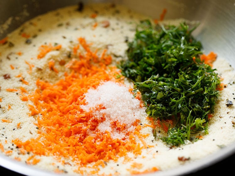cà rốt bào nhuyễn, lá rau mùi thái nhỏ và thêm muối vào rava trong chảo để làm suji ki idli.