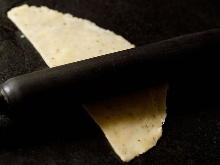 half of the cut dough being rolled lightly with a wooden rolling pin