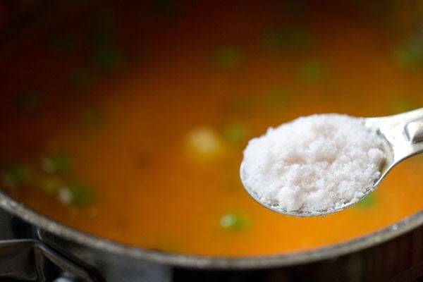 silver teaspoon of salt above pot of aloo matar