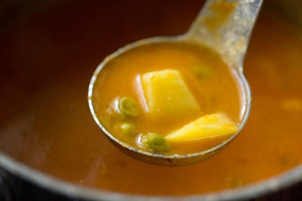 spoonful of potatoes and peas after simmering to show that potatoes are soft enough to split with a spoon