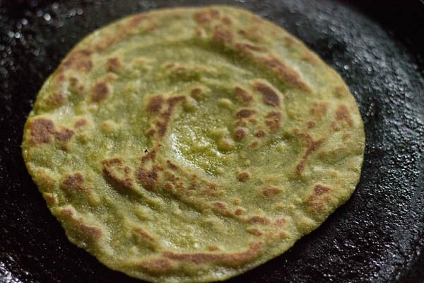 frying aloo palak paratha on a hot tawa.