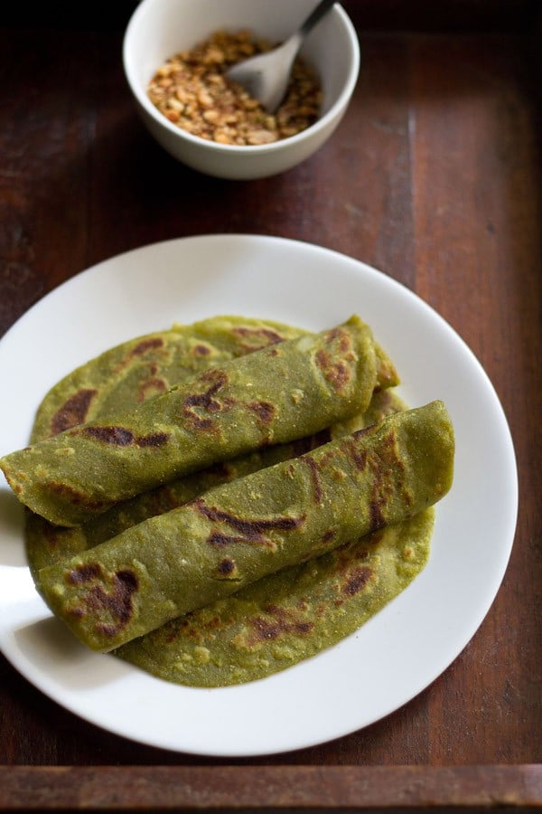 2 rolled aloo palak paratha kept on another paratha and served on a white serving plate.
