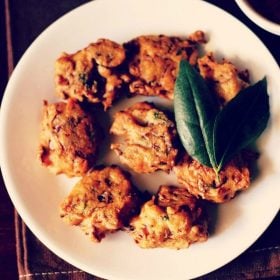 cabbage vada with a two leaf sprig of curry leaves served on a white plate