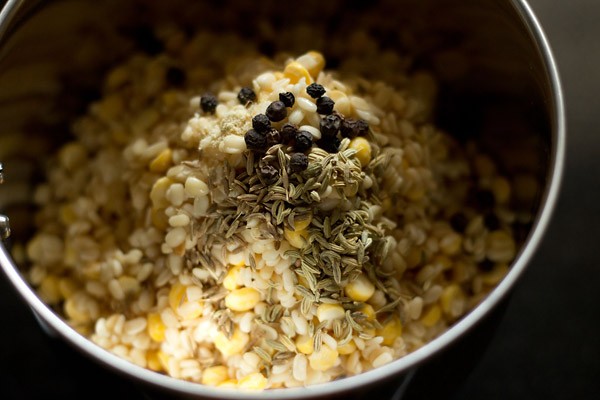 adding black pepper, fennel seeds, cumin seeds and asafoetida to lentils in grinder jar