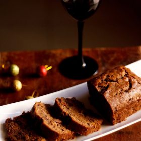 wine cake sliced and served on a white platter with a glass of red wine kept in the background.