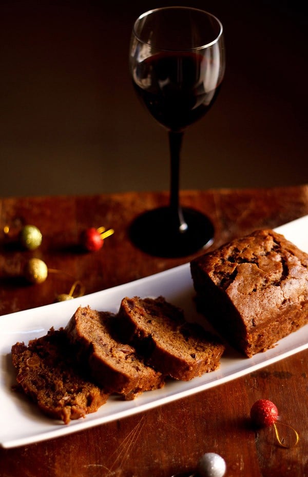 wine cake sliced and served on a white platter with a glass of red wine kept in the background.