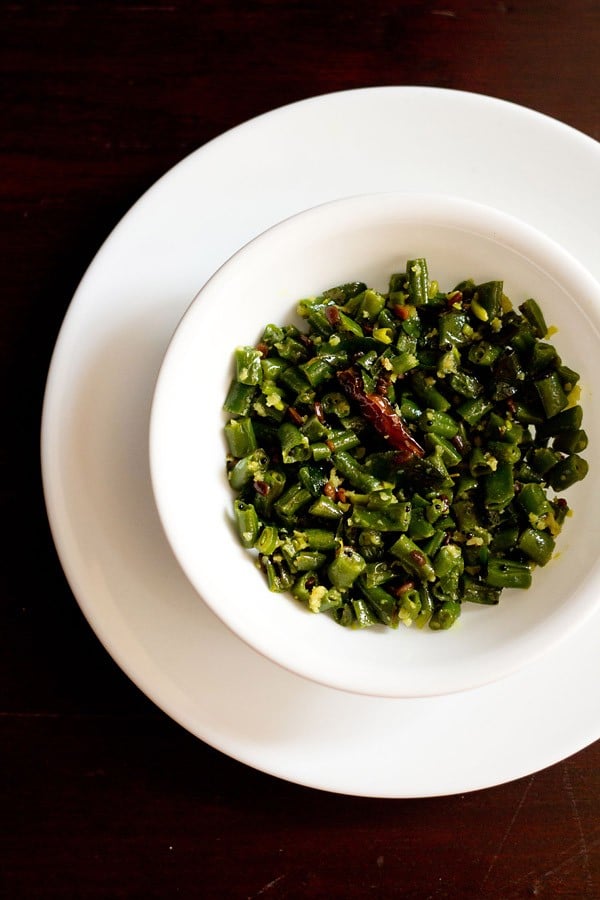 beans poriyal served in a white bowl placed on a white plate.