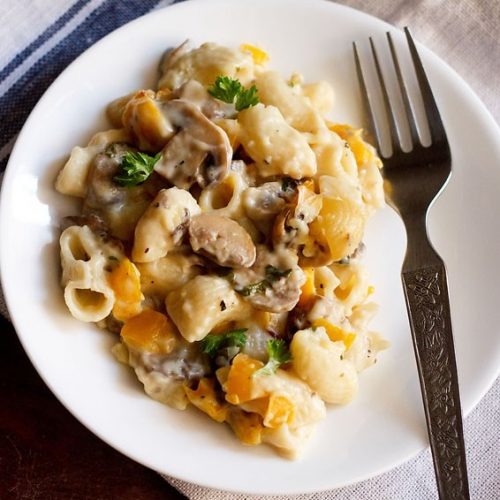 mushroom pasta served in a white plate with a steel fork at the side