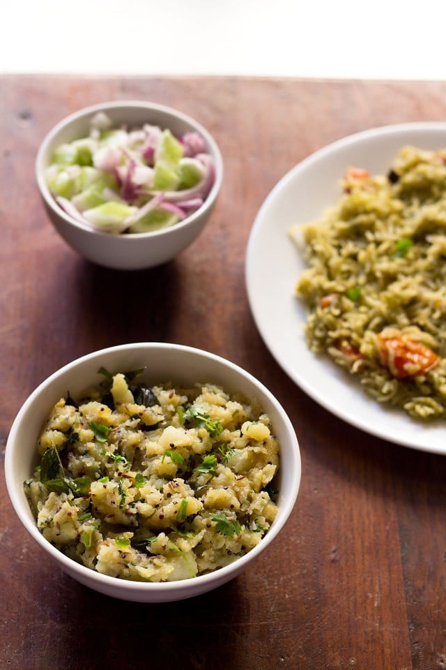 The potato pods were served in a white bowl with a plate of masala rice and a small bowl of cucumbers and onions. 