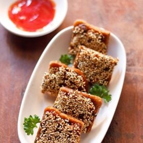 sesame toast garnished with coriander leaves and served on a white platter with red chili sauce.