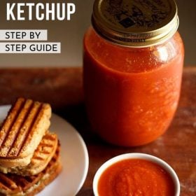 tomato ketchup served in white bowl next to a plate of grilled sandwiches and a mason jar of tomato sauce behind