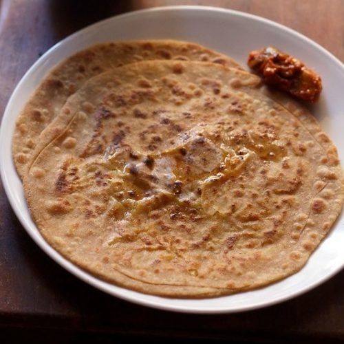 aloo gobi paratha on white plate with pickle by the side.